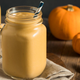 A glass of pumpkin coquito with pumpkins in the background